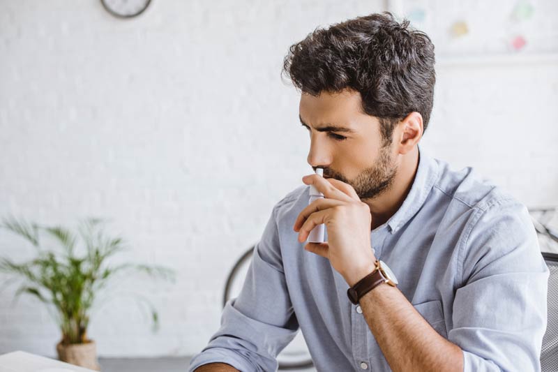 Sick Male using nasal spray in office