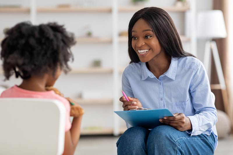 Smiling pretty black woman talking to a child about ear implants